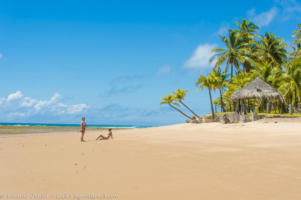 Imagem de duas moças na areia aproveitando esta vista pra Praia Taipu de Fora.